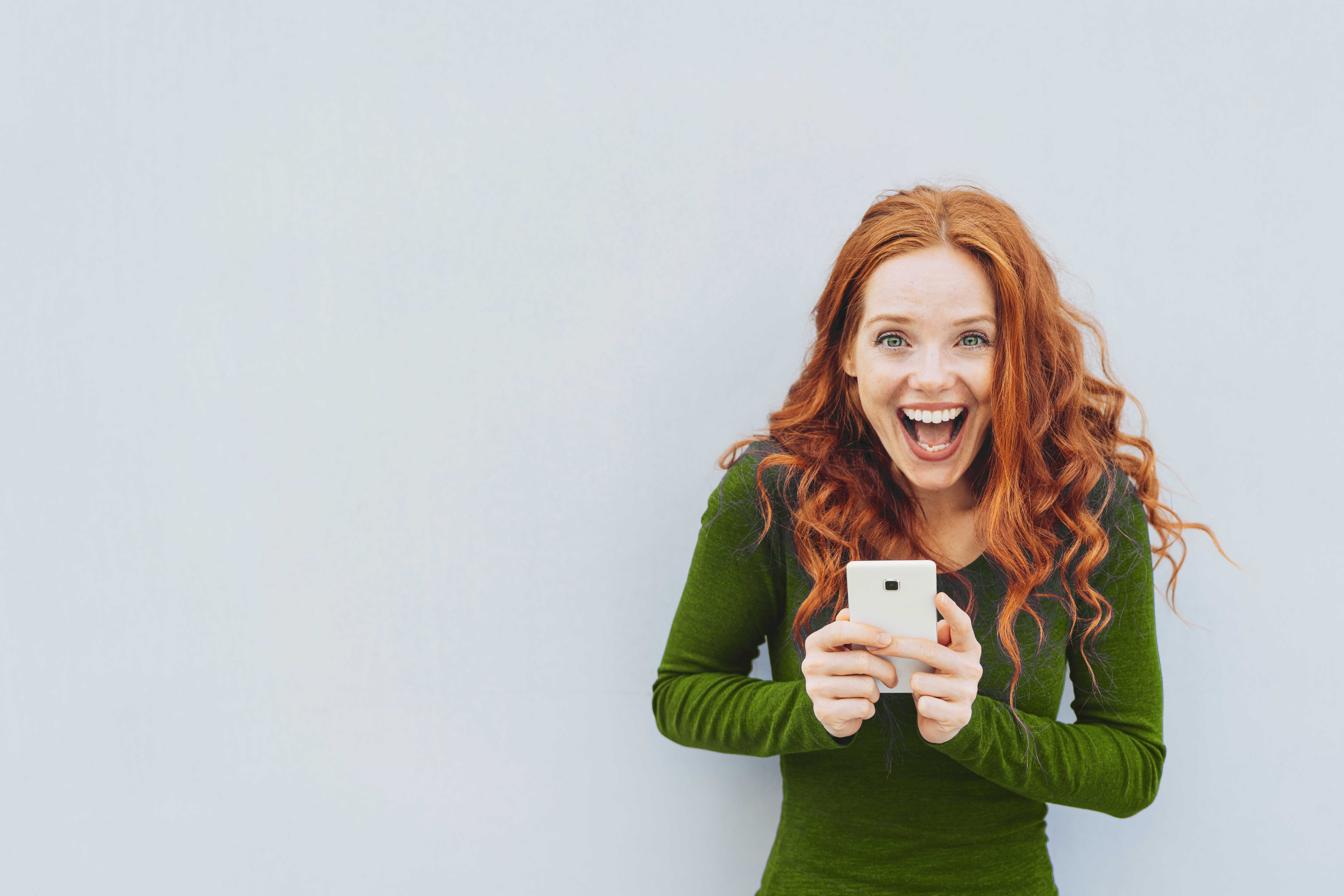 Eine Frau hält ein Handy in der Hand und blickt sehr glücklich in die Kamera