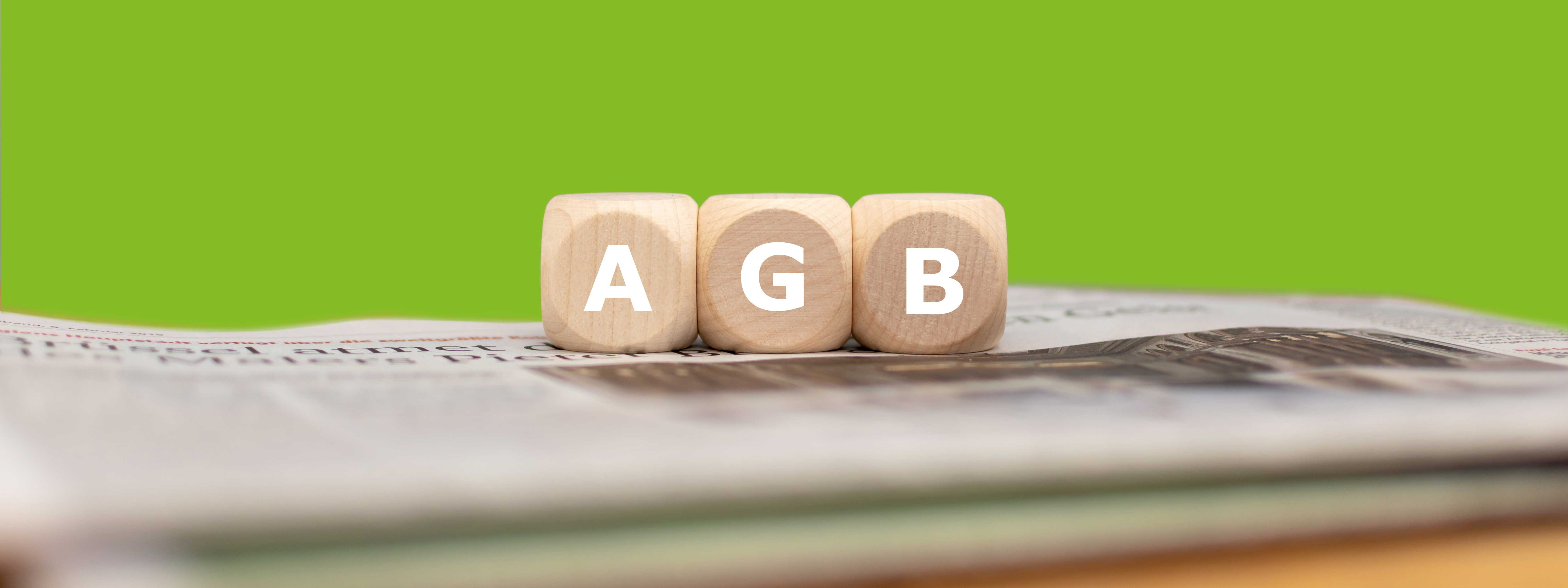Drei Würfel mit aufgedruckten Buchstaben, die zusammen die Abkürzung AGB ergeben, liegen auf einer Zeitung